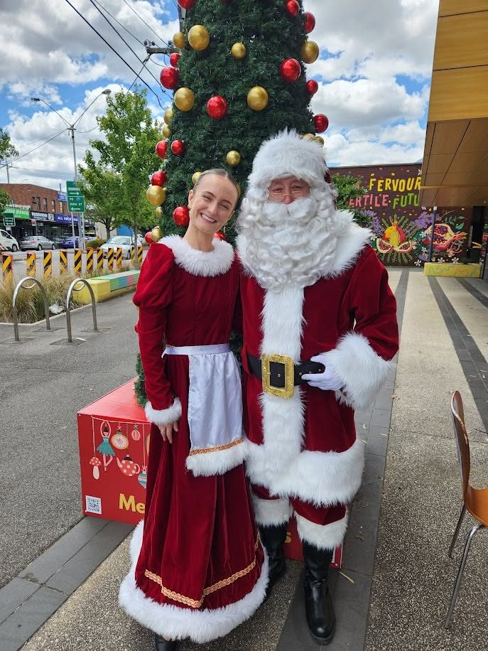 Santa and Mrs Claus beside an outdoor Christmas tree in a town centre