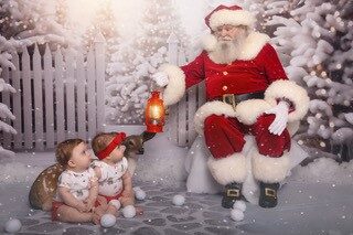Santa holding a lantern with two babies in a snowy scene